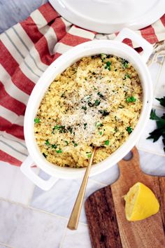 a casserole dish with parmesan cheese on top and lemon wedges next to it