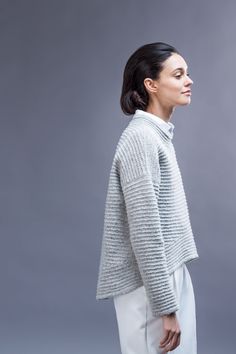 a woman standing in front of a gray background with her hand on her hip and looking off to the side