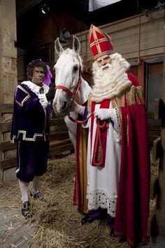 a man standing next to a white horse wearing a red and gold outfit with a person dressed as santa claus