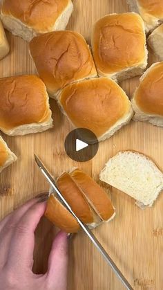 a person cutting bread with a knife on a wooden board next to other buns