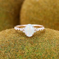 a white opal and diamond ring sitting on top of moss covered ground with grass in the background