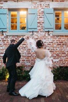 a bride and groom dancing together in front of a brick building with blue shutters