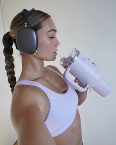 a woman with headphones on drinking from a cup while holding a hair dryer