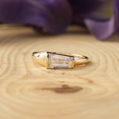 a yellow gold ring with a baguette cut diamond in the center on a wooden surface