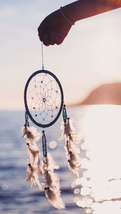 a person holding a dream catcher in their hand near the ocean with sun shining on it