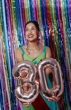 a woman is holding two large balloons in front of colorful streamers and the number 30