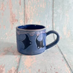 a blue coffee mug with two black fish on it's side sitting on a wooden surface