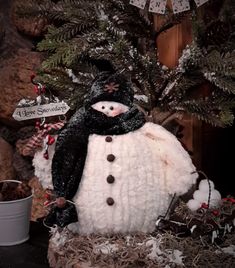 a snowman with a black hat and scarf is sitting in front of a christmas tree