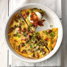 a pizza with meat, cheese and vegetables in a bowl on a white tablecloth