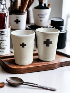 two cups with crosses on them are sitting on a tray next to bottles and spoons