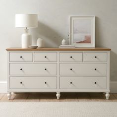 a white dresser with two lamps on top of it and a painting above the drawers