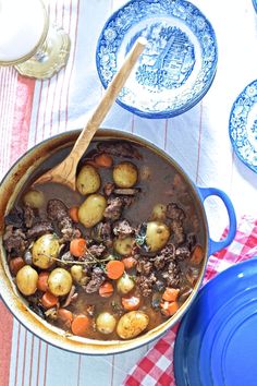 a pot filled with stew and potatoes on top of a table next to plates, glasses and utensils