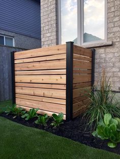 a wooden fence in front of a brick building with grass and plants growing around it