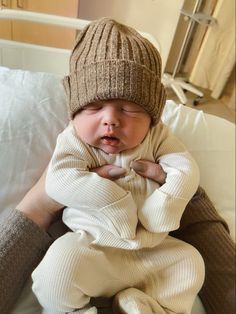 a newborn baby wearing a knitted hat and sleeping in a hospital bed with his hands on his chest