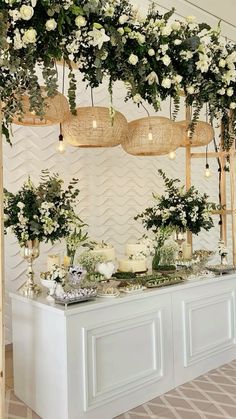 a table topped with lots of white flowers and greenery next to a wall covered in wicker baskets