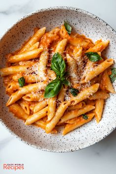 pasta with basil and parmesan cheese in a white bowl on a marble table