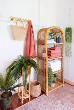 a bamboo shelf with towels and plants in it next to a potted plant on the floor