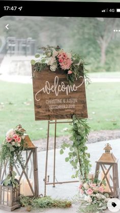 a wooden sign with flowers and greenery on it next to two small lanterns that read welcome