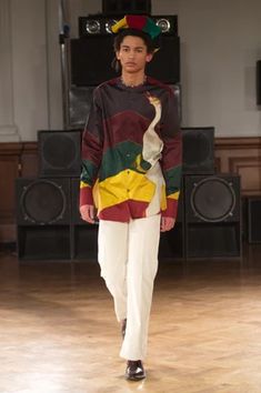 a woman is walking down the runway in white pants and a colorful shirt with an animal on it