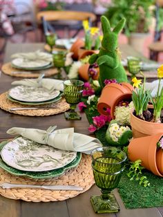 the table is set with plates, cups and vases filled with flowers on it