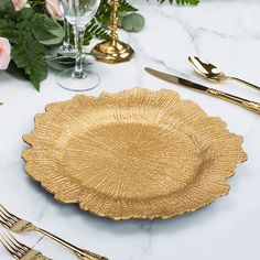 a gold plate sitting on top of a white table next to silverware and flowers