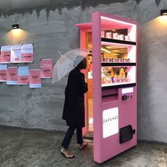 a woman with an umbrella is standing in front of a vending machine