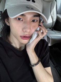 a woman wearing a baseball cap talking on a cell phone in the back seat of a car