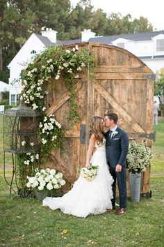 a bride and groom kissing in front of a wooden structure with white flowers on it