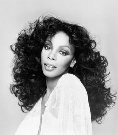 a black and white photo of a woman with long curly hair, wearing a blouse