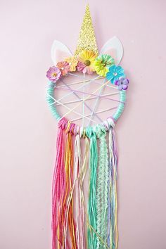 a wall hanging made out of yarn with a unicorn's horn on top and flowers in the middle