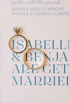 two gold wedding rings sitting on top of a white card with the words isbella and beja are get married