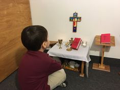 a young boy kneeling down in front of a small table with two candles on it