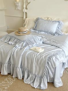 a bed with blue sheets and ruffled bedspread in a white bedroom setting