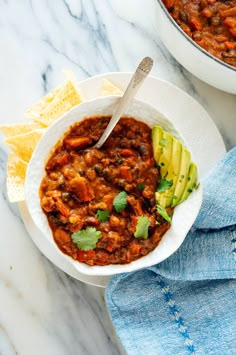 a white bowl filled with chili and avocado on top of a marble counter