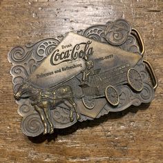 "Vintage Coca Cola raised design Horse and Delivery Carriage design brass colored belt buckle 1976 Bergamot. 1976 Bergamot Brass Works Coca Cola Company on back.  Metal composition unknown.  Small markings on buckle, as pictured.  Buckle measures approximately 3 3/4\" across x  2 3/4\" tall.  No belt included.  Buckle sold as-is, as pictured.  All Sales Final." Vintage Gold Belt Buckle With Antique Detail, Gold Antique Buckle Vintage Belt Buckles, Gold Antique Buckle Vintage Belt Buckle, Gold Antique Buckle Vintage Belt, Gold Vintage Belt Buckle With Antique Detail, Vintage Brown Belt Buckles With Brass Buckle, Vintage Brown Belt With Brass Buckle, Retro Vintage Brown Belt Buckle With Antique Detail, Vintage Gold Belt With Brass Hardware