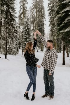 a man and woman standing in the snow with their hands up to each other,