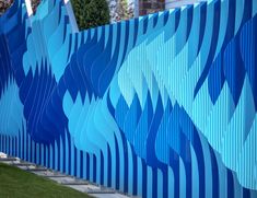 a blue and white fence with waves painted on the wall next to grass in front of a building