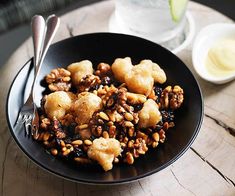 a black bowl filled with food on top of a wooden table next to a glass