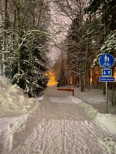 a snow covered road with trees and street signs in the distance, at night time