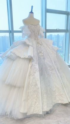 a white wedding dress is on display in front of a large window with city view