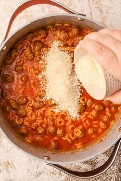 someone is grating cheese on top of some pasta in a large skillet with meatballs and sauce