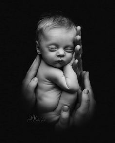 a black and white photo of a baby being held by its mother's hands