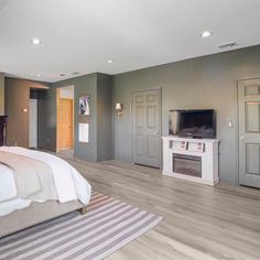 a bedroom with gray walls and white bedding has a flat screen tv on the wall