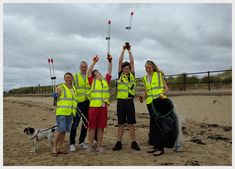 four people in yellow vests are holding up their sticks and bags on the beach