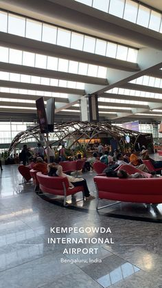 people are sitting on red couches in an airport lobby with large windows above them