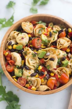 a wooden bowl filled with pasta salad and black olives, tomatoes, corn, avocado