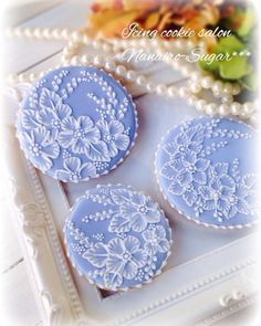 three blue decorated cookies sitting on top of a white tray next to a pearl necklace