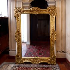 a large gold framed mirror sitting on top of a wooden floor next to a doorway