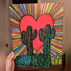 a hand holding up a painting with cactuses and a heart in the middle on it