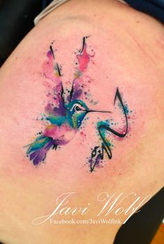 a colorful hummingbird tattoo on the back of a woman's stomach, with watercolor splashes